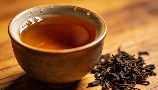 Ceramic cup of freshly brewed black tea with loose tea leaves scattered on a wooden surface