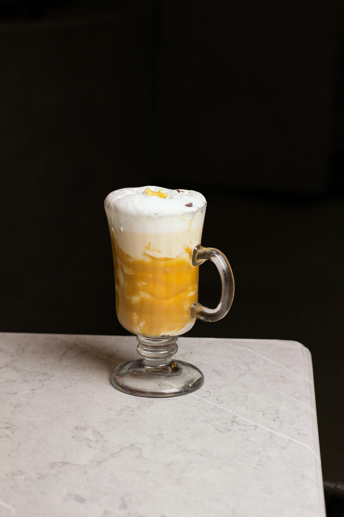 Iced mango cream chai latte in a tall glass with frothy mango cream on top, layered amber chai underneath